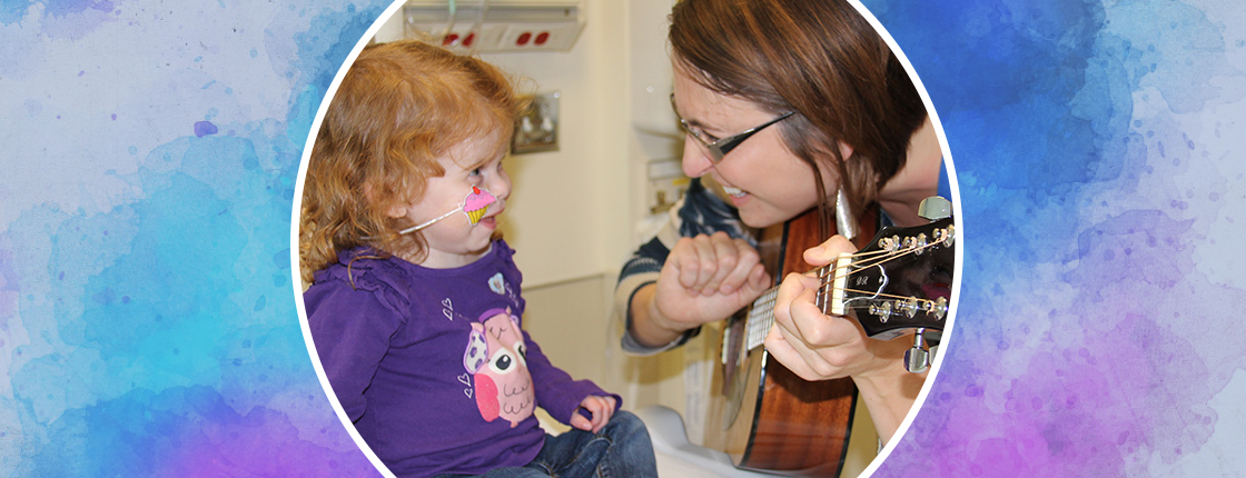Little girl smiles at Music Therapist playing guitar during music therapy.