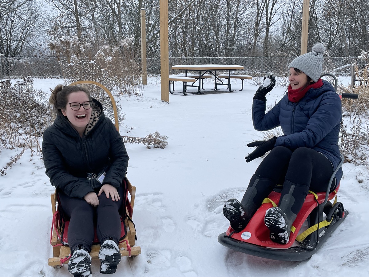 People smiling and sitting on sleds outside in winter.