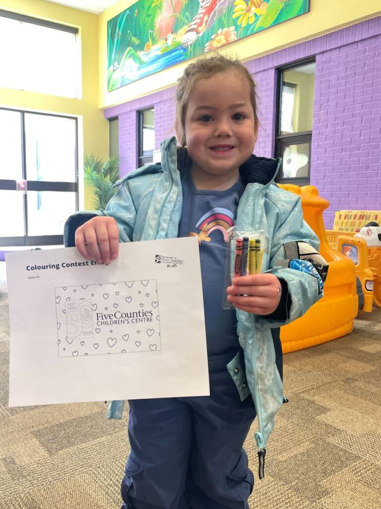 Little girl displays colouring sheets for contest.