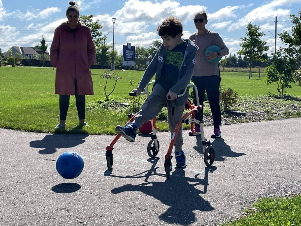 Boy with mobility device kicking soccer ball.